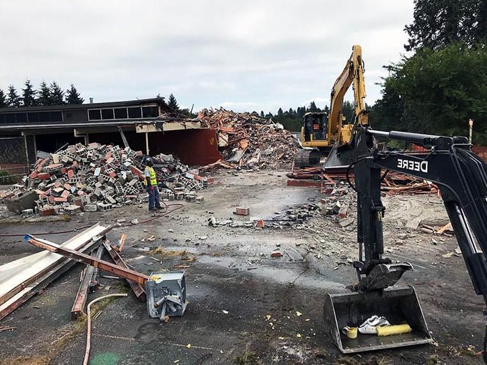 a demolition site with heavy equipment and piles of debris in front of a partially demolished building