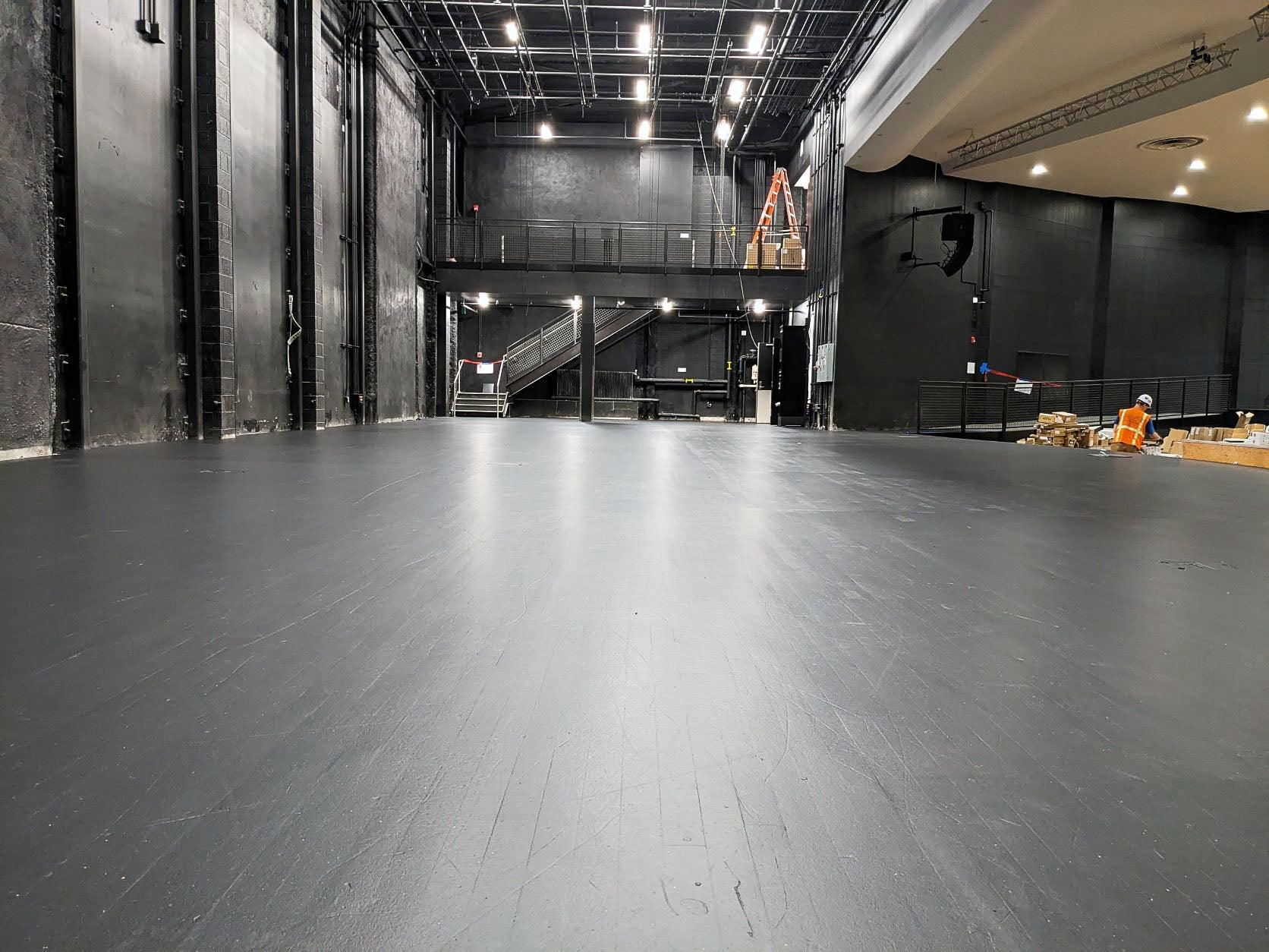 a black floor has black walls and theatre rigging lights above it