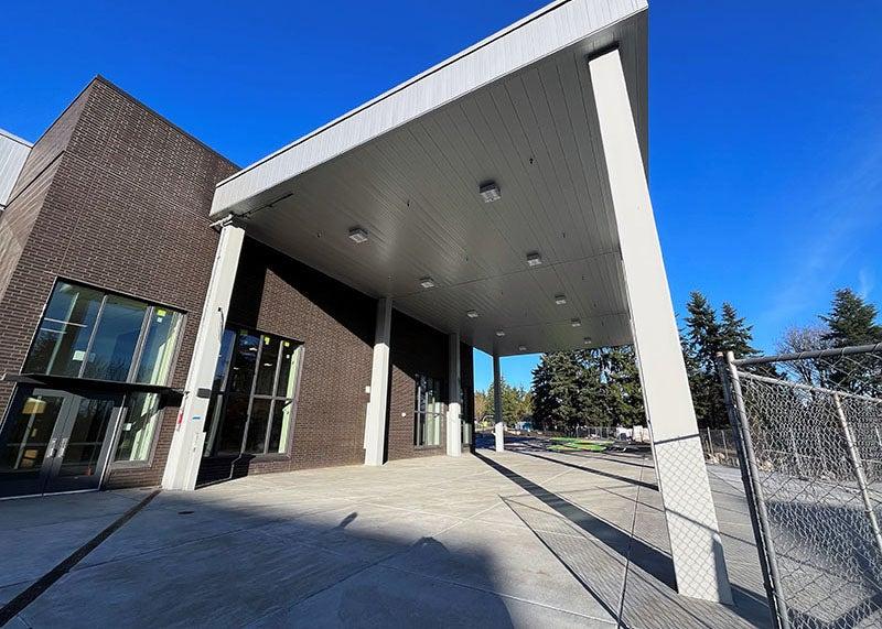 a concrete paved area next to a building has a roof on posts over it